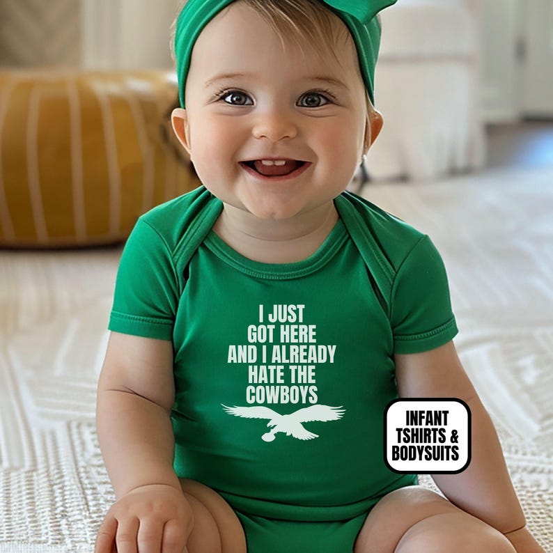 Puede incluir: Un body de manga corta para beb&eacute; en color verde con el texto blanco I JUST GOT HERE AND I ALREADY HATE THE COWBOYS sobre un gr&aacute;fico de &aacute;guila blanca. La prenda se combina con una cinta para el pelo verde a juego para beb&eacute;s.