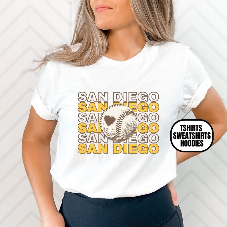 May include: White t-shirt with a graphic of a baseball with a heart on it and the text "SAN DIEGO" repeated in yellow letters.