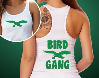 Könnte beinhalten: Ein weißes Racerback-Tanktop mit dem grünen Schriftzug BIRD GANG und einer grünen Adlergrafik. Das Design ist auf der Rückseite des Kleidungsstücks gedruckt, während ein kreisförmiger Einsatz die Vorderseite des Tanktops mit derselben Adlergrafik zeigt.