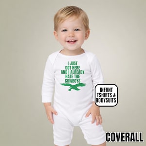 Puede incluir: Un body blanco de manga larga para beb&eacute; con texto verde que dice I JUST GOT HERE AND I ALREADY HATE THE COWBOYS sobre un gr&aacute;fico de &aacute;guila verde. La prenda incluye una peque&ntilde;a etiqueta rectangular con el texto INFANT TSHIRTS & BODYSUITS.