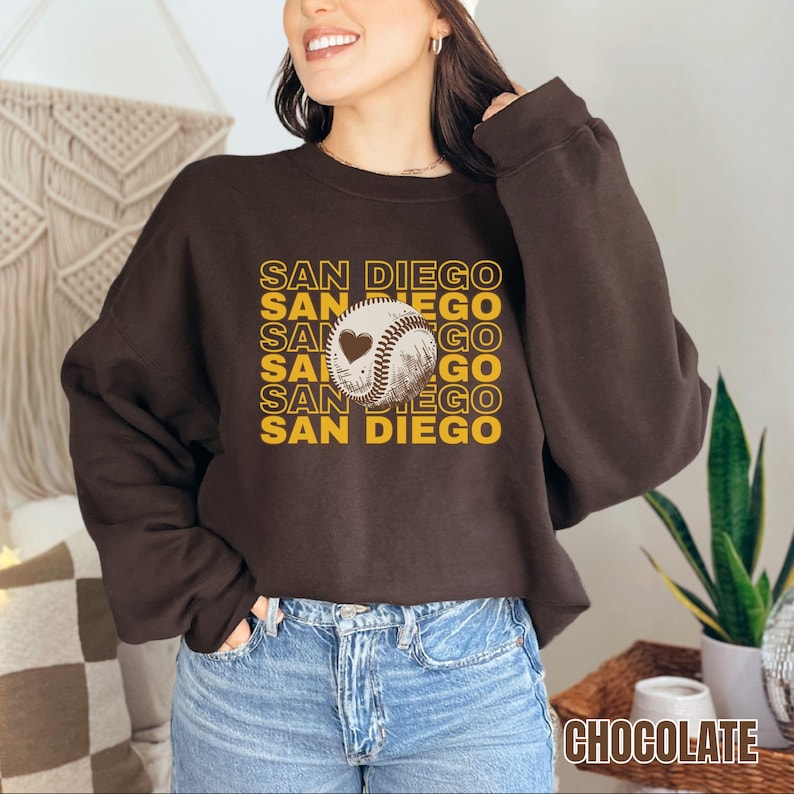 May include: A brown sweatshirt with a graphic of a baseball with a heart on it and the text "SAN DIEGO" repeated in a stacked pattern.