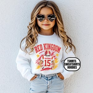 May include: A white long-sleeve sweatshirt featuring a graphic print of a football player wearing a jersey with the number 15 and the name Mahomes, with the text RED KINGDOM above, and a black circular badge with the text TSHIRTS SWEATSHIRTS HOODIES.