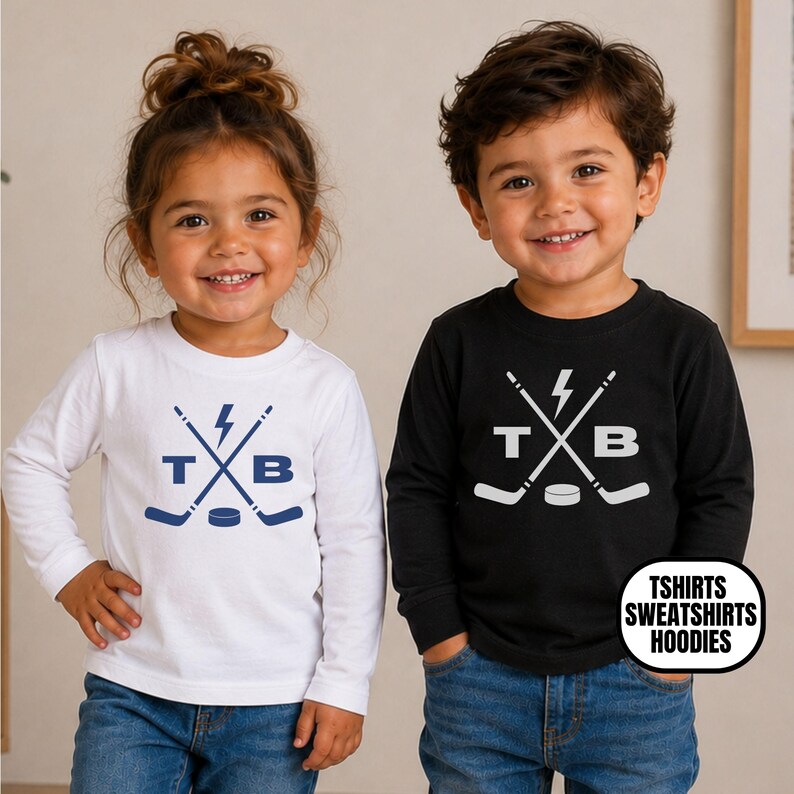 Pu&ograve; includere: Una maglietta bianca a maniche lunghe con una grafica blu di bastoni da hockey incrociati, un fulmine, un disco e le lettere T e B, e una maglietta nera a maniche lunghe con una grafica bianca dello stesso design, con il testo TSHIRTS SWEATSHIRTS HOODIES.