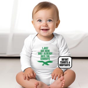 Puede incluir: Un body de manga larga para beb&eacute; en color blanco con texto verde que dice I JUST GOT HERE AND I ALREADY HATE THE COWBOYS sobre un gr&aacute;fico de un &aacute;guila verde. La prenda tiene un cuello redondo y mangas largas que cubren el torso superior.