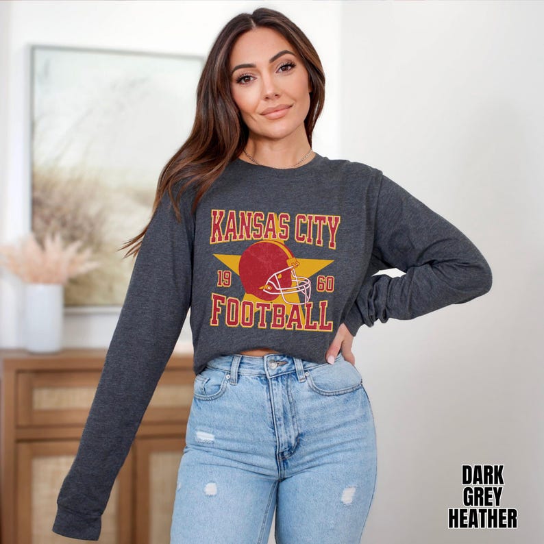 May include: A dark grey heather long-sleeve cropped sweatshirt with a vintage-style graphic of a football helmet and the text "Kansas City Football 19 60".