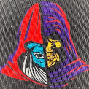 Puede incluir: Un parche negro con un diseño dividido de la cara de un personaje. Un lado muestra una figura de cara azul con una capucha roja, el otro una calavera amarilla con una capucha morada. El parche tiene una superficie texturizada.