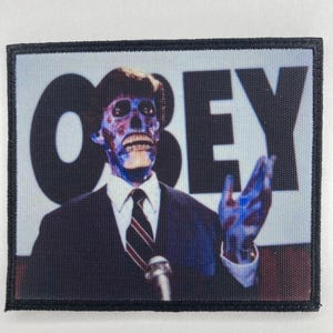 Könnte beinhalten: Rechteckiger Aufnäher mit einem blau getönten Bild eines Mannes im Anzug und dem Wort "OBEY" in Weiß. Der Mann hat ein skelettartiges Gesicht und spricht in ein Mikrofon.