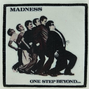 以下が含まれることがあります： マッドネスのバンドが描かれた正方形のパッチ。画像には、バンド名が上部に、"ONE STEP BEYOND..."が下部に表示され、バンドメンバーが並んでいます。パッチには黒い縁取りがあります。