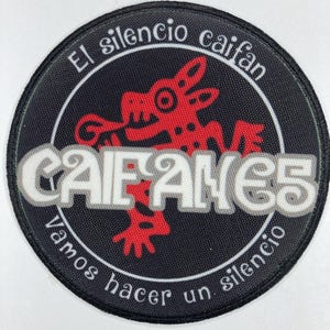Puede incluir: Un parche redondo negro con texto blanco y rojo. El texto incluye "El silencio caifan" y "CAIFANES" en una fuente estilizada. Un gráfico rojo de una criatura está en el centro. El parche también tiene el texto "Vamos hacer un silencio".