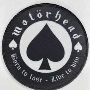 Puede incluir: Parche redondo negro con el texto "motörhead" en letras góticas blancas. Un símbolo de pica negro está centrado sobre un fondo blanco. El texto "Born to lose - Live to win" está impreso alrededor de la pica.