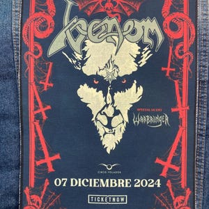 Puede incluir: Un parche de tela rectangular con fondo azul oscuro y gráficos en rojo y blanco hueso. Muestra el texto Venom, Warbringer y 07 Diciembre 2024. Una cinta métrica en la parte superior indica un ancho de aproximadamente 25,4 cm.