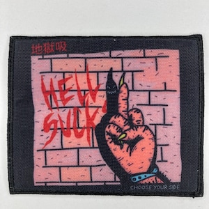 Könnte beinhalten: Ein rechteckiger Aufnäher mit schwarzem Rand. Das Design zeigt eine Cartoon-Hand mit langen, scharfen Nägeln, die den Mittelfinger zeigt. Der Hintergrund ist eine Backsteinmauer mit den Worten "HELL SUCK" in Rot. Der Text "CHOOSE YOUR SIDE" steht unten.
