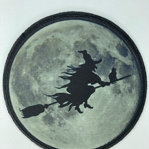 Puede incluir: Un parche bordado en blanco y negro de una bruja volando en una escoba frente a una luna llena.