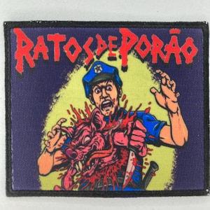 Peut inclure: Un écusson rectangulaire avec le texte "RATOS DE PORÃO" en rouge. L'image représente une personne en uniforme de policier avec un couteau, entourée de sang et d'une créature rose. Le fond est un mélange de jaune et de violet.