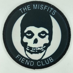 Puede incluir: Un parche bordado circular que presenta un gráfico en blanco y negro de una calavera con capucha. El texto THE MISFITS está arqueado en la parte superior y el texto FIEND CLUB está arqueado en la parte inferior, sobre un fondo circular blanco.