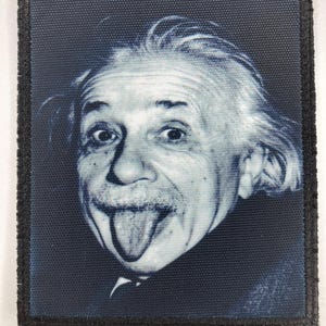 May include: A rectangular fabric patch featuring a monochromatic blue and white photographic print of Albert Einstein with his tongue sticking out. The patch has a dark blue border with a visible woven texture throughout the entire surface.