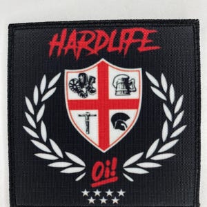 May include: A square black fabric patch featuring the red text HARDLIFE at the top and Oi! at the bottom. A central shield displays a red cross on white with four icons: boots, a beer mug, a cross, and a helmet, flanked by white laurel leaves.