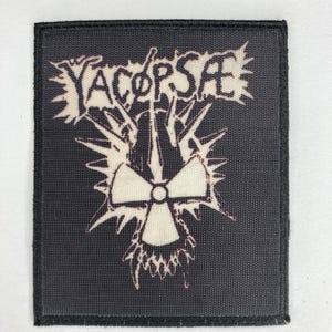 Może przedstawiać: Czarno-biała naszywka haftowana z tekstem "YACøPSÆ" i stylizowanym symbolem promieniowania.