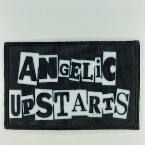 May include: A rectangular black patch with the words "ANGELIC UPSTARTS" in a white, cut-out style font. The patch has a black border and is set against a white background.