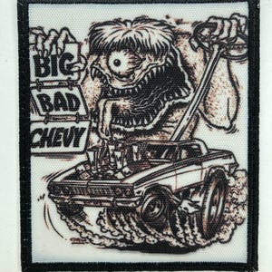 Op de afbeelding: Een rechthoekige geborduurde patch met een zwarte rand met een zwart-witte illustratie van een eenogig monster dat een bord vasthoudt met de tekst BIG BAD CHEVY. Het monster is afgebeeld terwijl het een klassieke auto bestuurt.