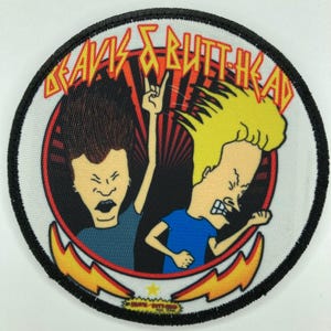 Puede incluir: Un parche bordado circular con los personajes de dibujos animados Beavis y Butt-Head. El diseño incluye el texto Beavis and Butt-Head en letras amarillas, un fondo de rayos de sol rojo y negro, y dos rayos amarillos en la parte inferior.