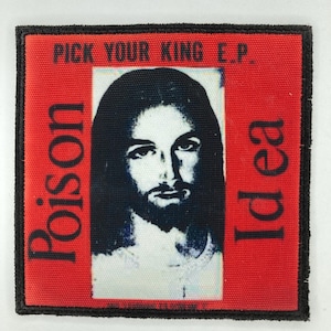 Puede incluir: Un parche de tela cuadrado con un borde cosido en negro. El fondo es rojo con el texto PICK YOUR KING E.P. en la parte superior, Poison a la izquierda e Idea a la derecha. Se muestra un retrato central en blanco y negro de una figura barbuda.