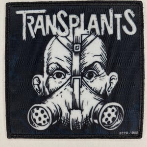 May include: Square patch with the word "TRANSPLANTS" in white, above a black and white illustration of a person wearing a gas mask. The patch has a black border and a dark blue background.