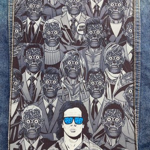 May include: A rectangular fabric patch featuring a black and white graphic illustration of multiple skull-faced figures in suits, with one central figure wearing blue sunglasses that read OBEY. The patch is stitched onto a blue denim jacket.