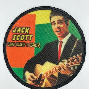 Puede incluir: Un parche redondo y colorido con un borde negro. Presenta una foto de Jack Scott, un hombre con cabello oscuro, que lleva un traje negro y una corbata roja, tocando una guitarra. El texto "JACK SCOTT THE WAY I WALK" está impreso en el parche.