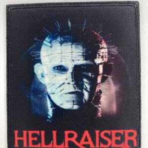 Puede incluir: Un parche cuadrado negro con un retrato de un personaje de la película Hellraiser. La cara del personaje está dividida, con tonos azules y rojos. La palabra "HELLRAISER" está impresa en rojo en la parte inferior.