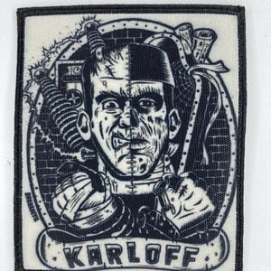 Könnte beinhalten: Schwarz-weißer Aufnäher mit einem stilisierten Bild von Frankensteins Monster. Das Design enthält den Namen "KARLOFF" in einem Banner am unteren Rand, umgeben von Schrauben, Werkzeugen und einem Backsteinmauer-Hintergrund. Der Aufnäher hat einen schwarzen Rand.