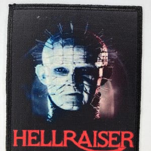 May include: Black fabric patch featuring a white and red image of a monster with a pin head and the text "HELLRAISER" in red.