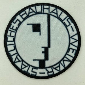 May include: Round patch with the Bauhaus logo in black and white. The design incorporates geometric shapes and the text "STAATLICHES BAUHAUS WEIMAR" in a circular arrangement. The patch is edged with a black border.
