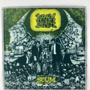 Könnte beinhalten: Ein quadratischer Stoffaufnäher mit einem grünen und schwarzen Grafikdruck. Das Design zeigt den Text Napalm Death oben und Scum unten, mit einem zentralen Bild von Figuren in Anzügen, umgeben von einer Menschenmenge und einem großen gelben Kreis.
