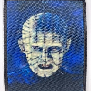May include: A black and blue embroidered patch featuring a close-up of a character with a stitched-up face and a menacing expression.