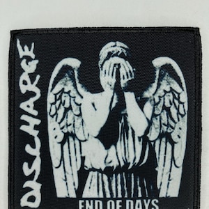 Puede incluir: Parche bordado en blanco y negro con el nombre de la banda "DISCHARGE" y el texto "END OF DAYS". El parche presenta una imagen estilizada de un ángel con la cara cubierta por sus manos.