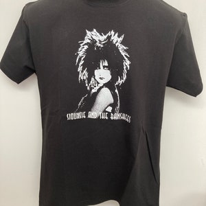 May include: Black t-shirt featuring a white graphic of Siouxsie Sioux from the band Siouxsie and the Banshees.