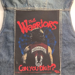 May include: A blue denim vest featuring a large rectangular black patch on the back. The patch displays a graphic of a person in a vest with the text THE WARRIORS in red, a blue Ferris wheel, and the red text CAN YOU DIG IT? at the bottom.