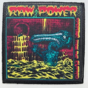 Könnte beinhalten: Quadratischer Aufnäher mit dem Text "RAW POWER" in Rot, über einem Design einer türkisfarbenen und schwarzen Kreatur. Der Hintergrund zeigt ein gelbes und rotes lavaartiges Muster mit einem schwarzen Rand.
