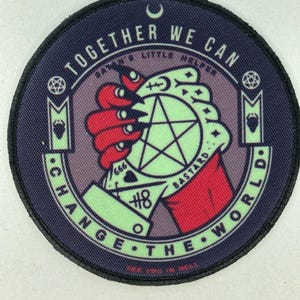 Puede incluir: Un parche circular con el texto "TOGETHER WE CAN CHANGE THE WORLD". El diseño presenta una mano roja sosteniendo un pentagrama verde, con las palabras "BASTARD" y el número "666".