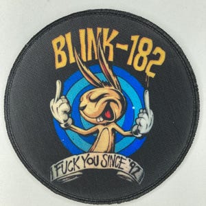 Puede incluir: Un parche redondo negro con un conejo de dibujos animados haciendo una peineta. El parche tiene el texto "BLINK-182" en amarillo y "FUCK YOU SINCE '92" en una pancarta. El conejo está frente a círculos concéntricos azules.