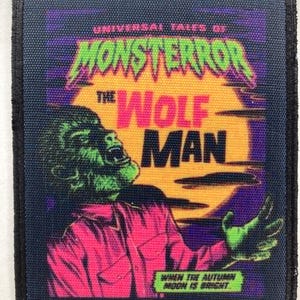 Puede incluir: Un parche cuadrado con borde negro, con un diseño retro de cómic. El parche muestra un hombre lobo verde con el texto "MONSTEROR THE WOLF MAN" en verde y naranja. También está presente el texto "UNIVERSAL TALES OF" y "WHEN THE AUTUMN MOON IS BRIGHT".