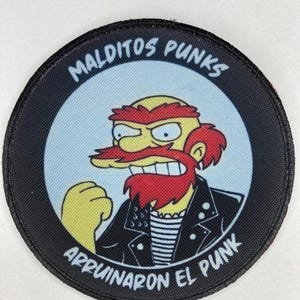 Può includere: Un cerotto circolare bianco e nero con un personaggio dei cartoni animati che indossa una giacca di pelle nera e una barba rossa. Il testo "Malditos Punks" è scritto in un cerchio attorno al personaggio e il testo "Arruinaron El Punk" è scritto sotto il personaggio.