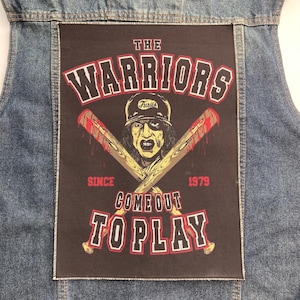 May include: A blue denim vest featuring a large rectangular black patch on the back. The patch displays a graphic of a person in a baseball cap with two crossed baseball bats, the text THE WARRIORS, SINCE 1979, and COME OUT TO PLAY.