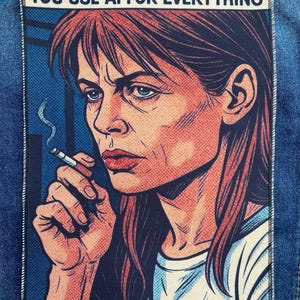 May include: A rectangular fabric patch featuring a comic-style illustration of a woman with long brown hair holding a lit cigarette. The text at the top reads: SARAH CONNOR WATCHING YOU USE AI FOR EVERYTHING. The patch is sewn onto blue denim fabric.