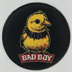Puede incluir: Un parche bordado negro y amarillo con un pollito de dibujos animados que lleva un collar con tachuelas y el texto "BAD BOY" en una pancarta roja.