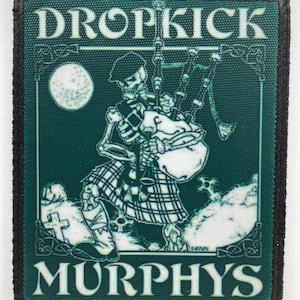 Puede incluir: Un parche rectangular bordado con fondo verde oscuro y borde negro. El diseño muestra un esqueleto con kilt y boina escocesa tocando la gaita en un cementerio. El texto DROPKICK MURPHYS está impreso en color blanco.
