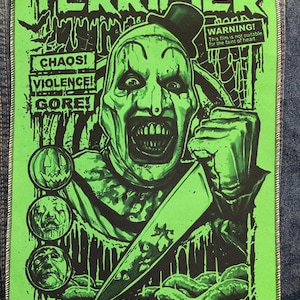 May include: A rectangular fabric patch featuring a bright green and black graphic print of the horror film Terrifier. The design includes the clown character Art, a large knife, three circular icons, and text reading A FILM BY DAMIEN LEONE.