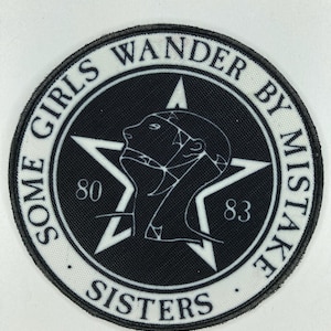 Puede incluir: Un parche redondo en blanco y negro con el texto "SOME GIRLS WANDER BY MISTAKE SISTERS" que rodea una estrella negra. Dentro de la estrella hay un perfil de una cabeza y los números "80" y "83".