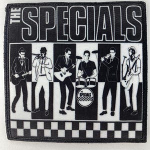 Op de afbeelding: Een zwart-wit patch met de band "The Specials". Het ontwerp bevat de naam van de band boven een dambordpatroon. Daaronder staan silhouetten van de bandleden die instrumenten bespelen.